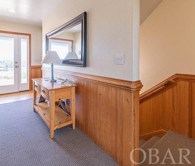 hallway featuring a wainscoted wall and dark colored carpet