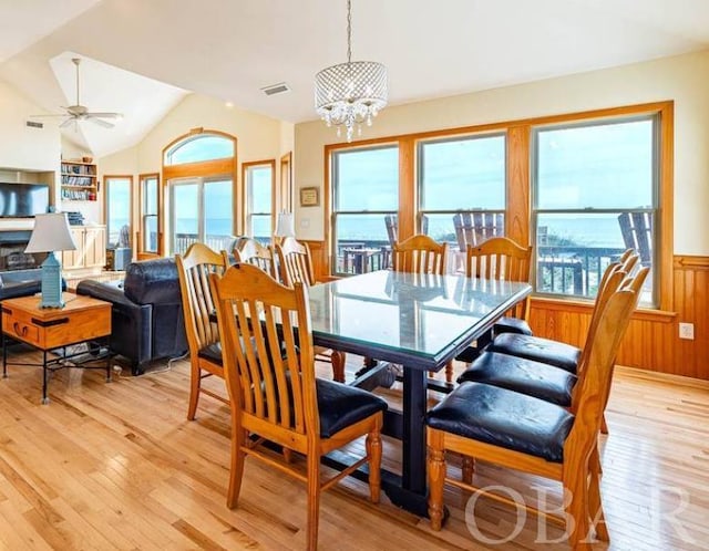 dining room with a wainscoted wall, vaulted ceiling, light wood-type flooring, and visible vents