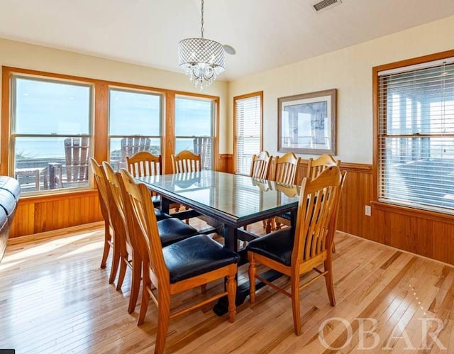 dining space featuring light wood finished floors, visible vents, wainscoting, wood walls, and a chandelier