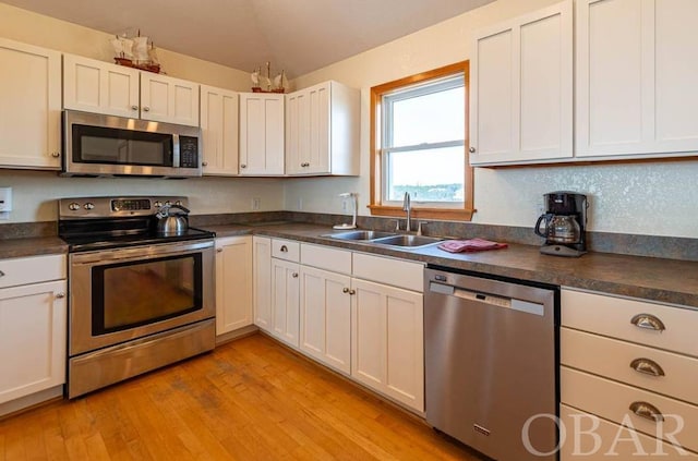 kitchen featuring stainless steel appliances, dark countertops, a sink, and white cabinetry