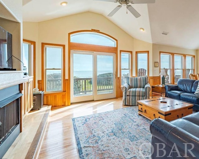 living area featuring lofted ceiling, wainscoting, light wood-style flooring, and a healthy amount of sunlight