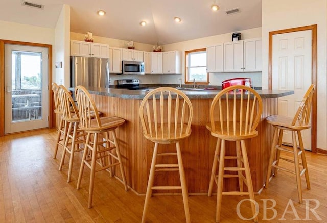 kitchen with white cabinets, dark countertops, a kitchen island, appliances with stainless steel finishes, and a kitchen breakfast bar