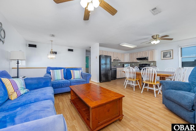 living room with light wood-style flooring, visible vents, and ceiling fan with notable chandelier