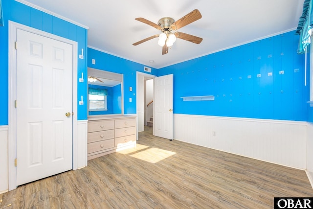 unfurnished bedroom with a wainscoted wall, crown molding, a ceiling fan, and wood finished floors