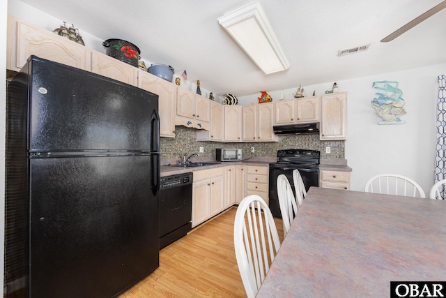 kitchen featuring light wood finished floors, visible vents, under cabinet range hood, black appliances, and a sink