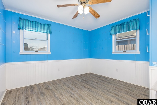 unfurnished room with ornamental molding, wainscoting, wood finished floors, and a ceiling fan