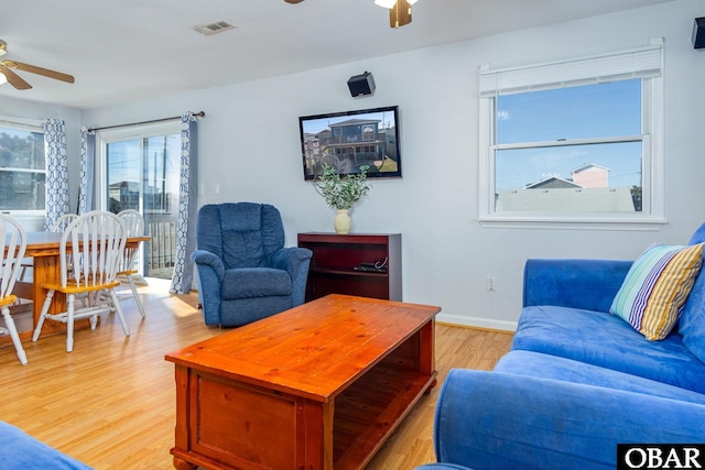 living area featuring baseboards, light wood-type flooring, visible vents, and a ceiling fan