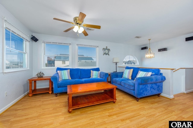 living room with light wood-style flooring, baseboards, and ceiling fan with notable chandelier