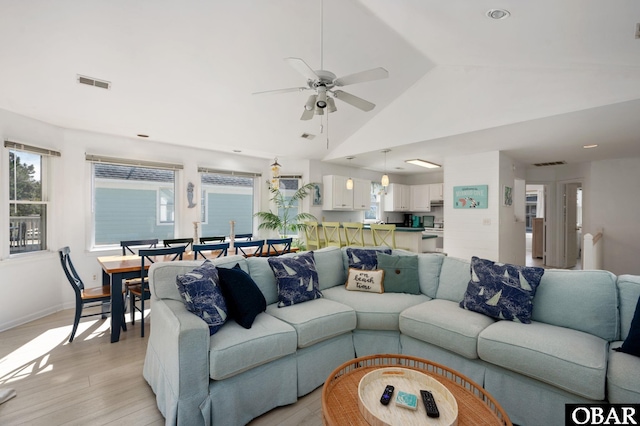 living room with light wood-type flooring, baseboards, visible vents, and vaulted ceiling