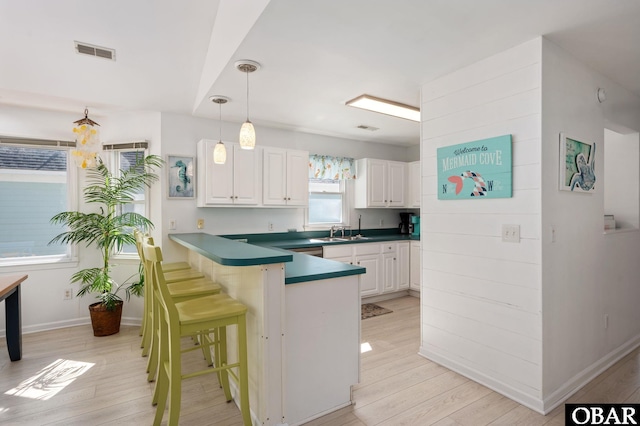 kitchen with pendant lighting, visible vents, white cabinets, a sink, and a peninsula