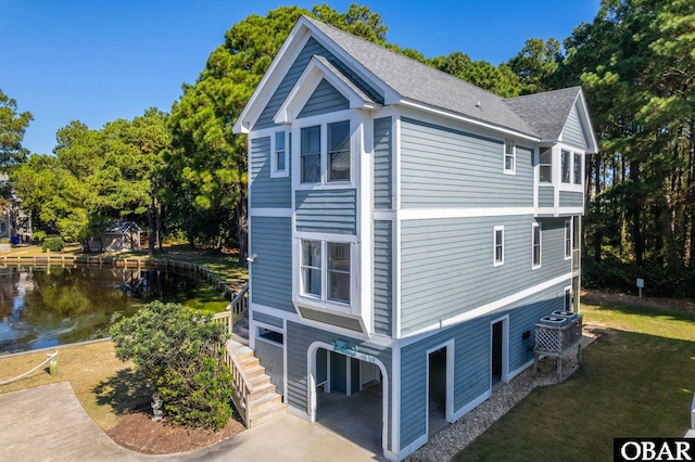 view of side of home with a water view, a shingled roof, stairs, and a garage