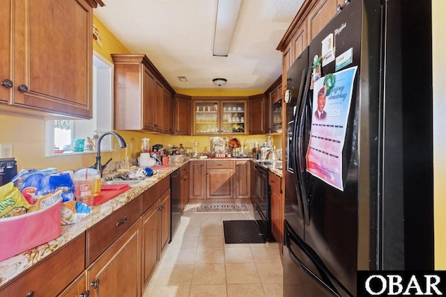 kitchen featuring brown cabinets, light stone countertops, black appliances, a sink, and light tile patterned flooring