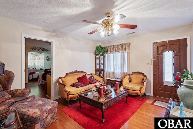 living room featuring baseboards, visible vents, a ceiling fan, wood finished floors, and a textured ceiling