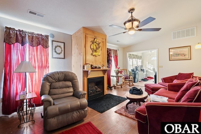 living room featuring lofted ceiling, visible vents, wood finished floors, and a glass covered fireplace