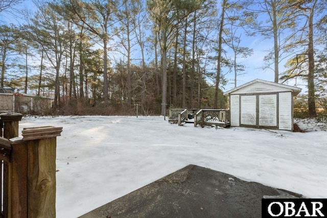 yard covered in snow featuring an outbuilding, a storage unit, and a deck