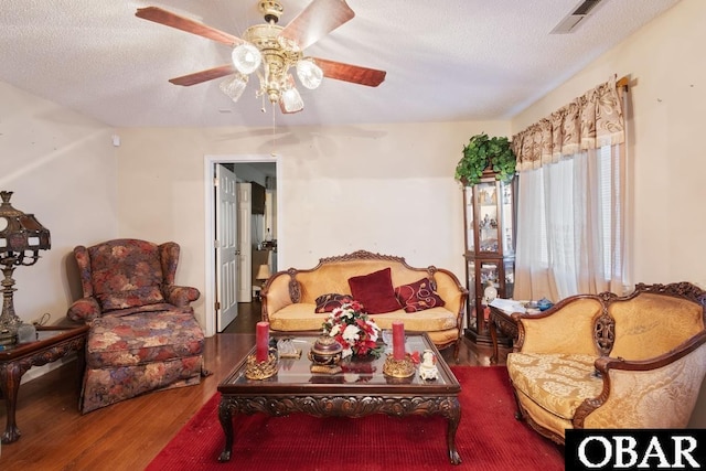 living area with a ceiling fan, visible vents, a textured ceiling, and wood finished floors