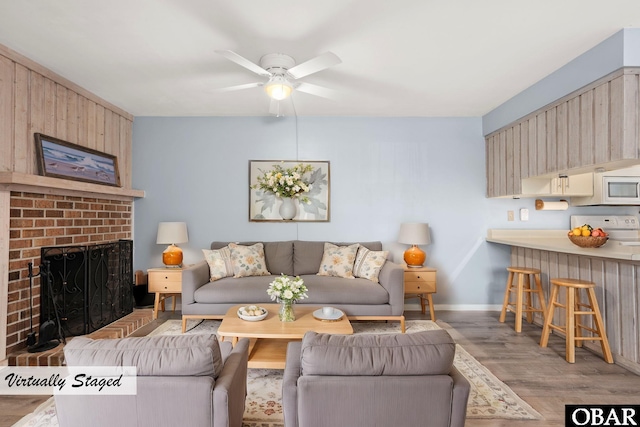 living area with a ceiling fan, a fireplace, baseboards, and wood finished floors