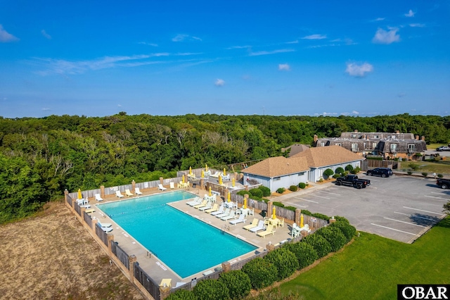 community pool featuring a wooded view, a patio area, and fence