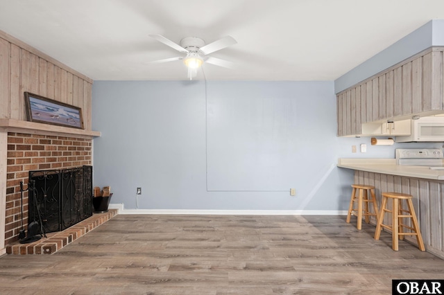 unfurnished living room with a fireplace, light wood-style flooring, baseboards, and ceiling fan