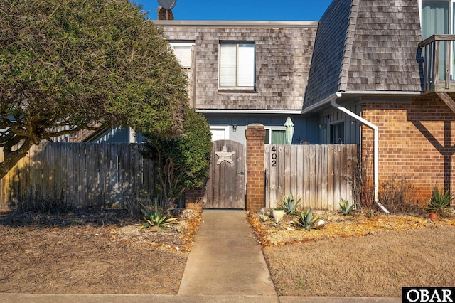 view of front of home with mansard roof, roof with shingles, a gate, fence, and brick siding