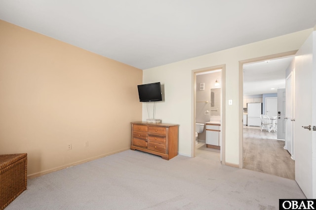 bedroom with freestanding refrigerator, light colored carpet, baseboards, and ensuite bathroom