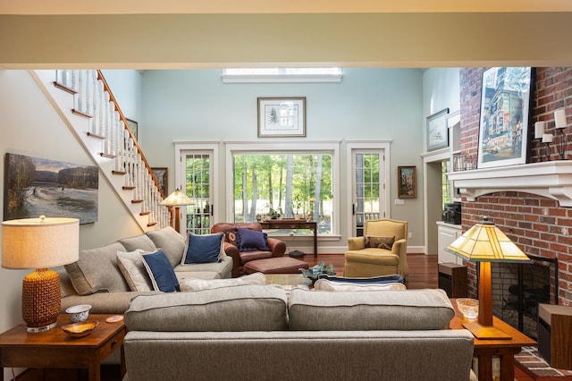 living area with stairs, a brick fireplace, wood finished floors, and a high ceiling