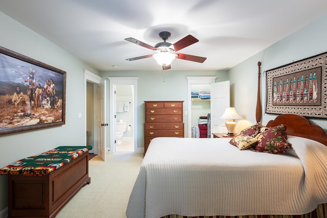 bedroom featuring light carpet, connected bathroom, baseboards, ceiling fan, and a spacious closet