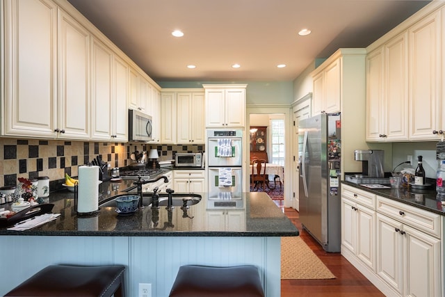 kitchen featuring a sink, backsplash, appliances with stainless steel finishes, a peninsula, and dark wood-style flooring