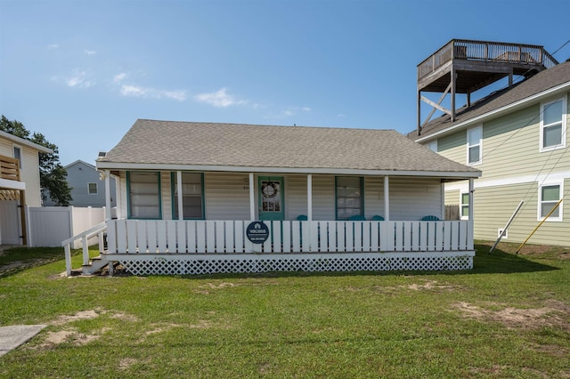 view of front of property with covered porch, roof with shingles, a front yard, and fence