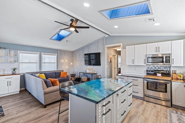 kitchen with visible vents, white cabinets, open floor plan, appliances with stainless steel finishes, and a kitchen bar