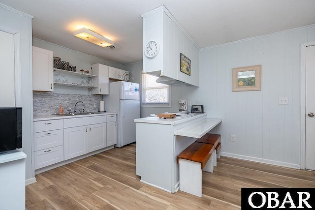 kitchen featuring light wood-type flooring, a sink, freestanding refrigerator, a peninsula, and light countertops