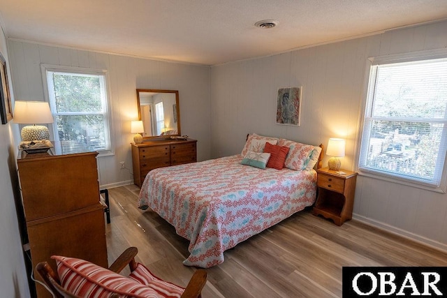 bedroom with crown molding, multiple windows, wood finished floors, and visible vents