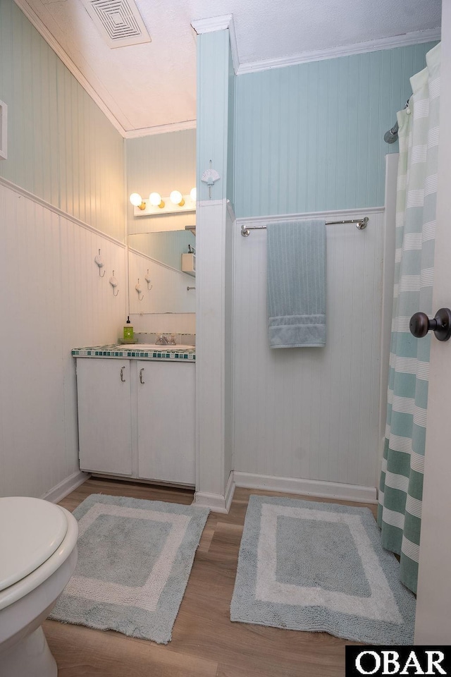 full bathroom with a shower with shower curtain, wood finished floors, visible vents, and ornamental molding