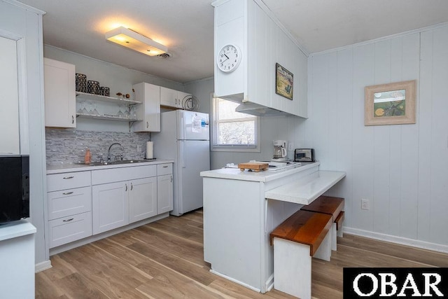 kitchen with a sink, light countertops, a peninsula, freestanding refrigerator, and open shelves