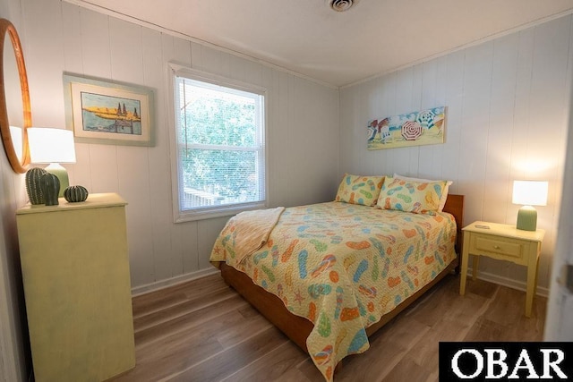 bedroom featuring visible vents, baseboards, wood finished floors, and crown molding