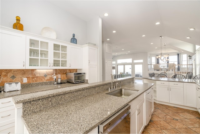 kitchen with a sink, white cabinets, glass insert cabinets, dishwasher, and a chandelier