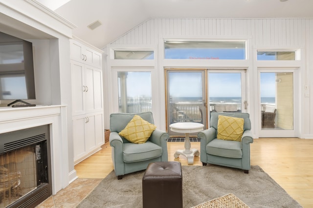 sitting room with visible vents, light wood-style flooring, a fireplace with flush hearth, and vaulted ceiling