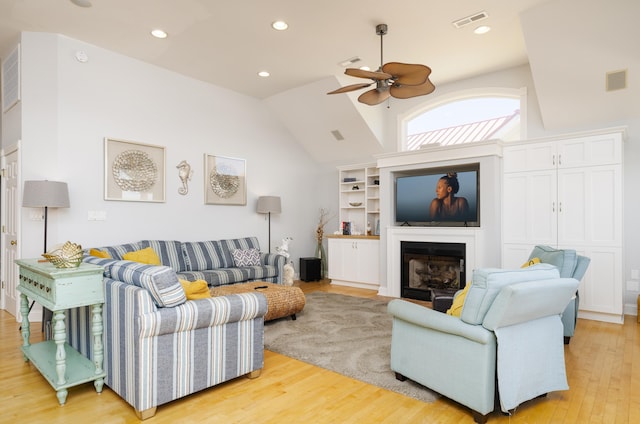 living area featuring visible vents, lofted ceiling, light wood-style flooring, a fireplace, and ceiling fan