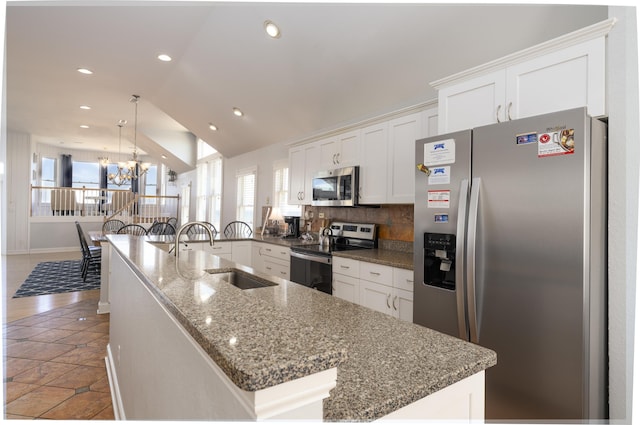 kitchen with lofted ceiling, a sink, appliances with stainless steel finishes, white cabinetry, and a chandelier