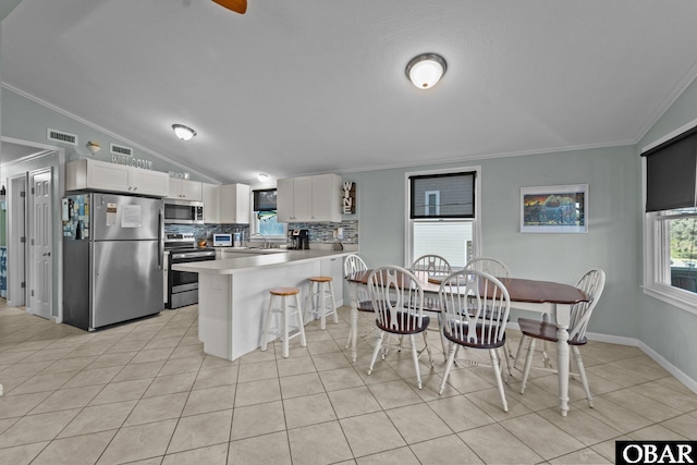 kitchen with lofted ceiling, a breakfast bar area, stainless steel appliances, white cabinetry, and light countertops