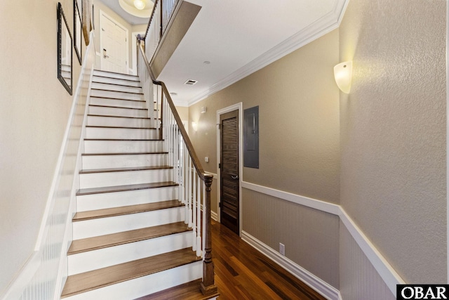 staircase featuring a wainscoted wall, crown molding, visible vents, wood finished floors, and electric panel