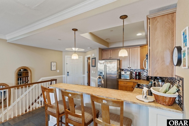 kitchen with a tray ceiling, stainless steel appliances, hanging light fixtures, backsplash, and a peninsula