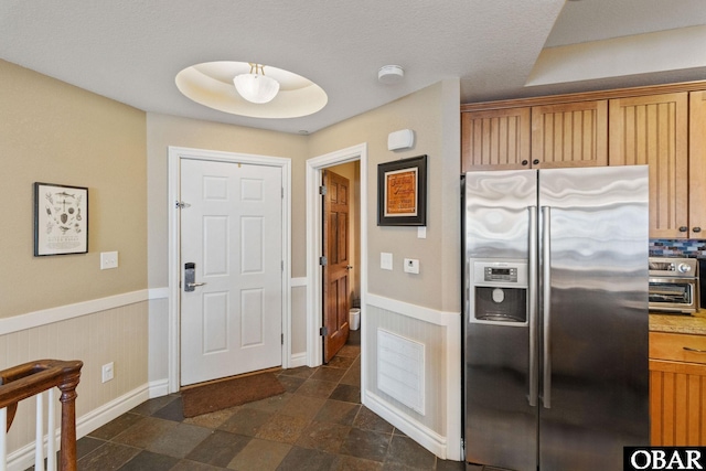 kitchen featuring a toaster, a wainscoted wall, stone finish floor, and stainless steel fridge with ice dispenser