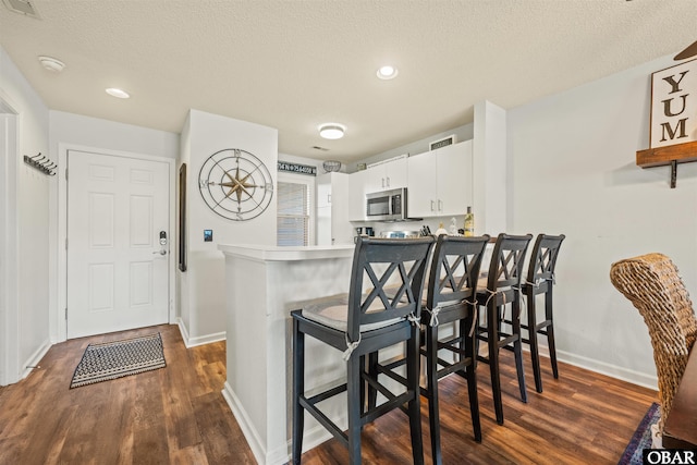 kitchen with a peninsula, a breakfast bar, white cabinets, light countertops, and stainless steel microwave