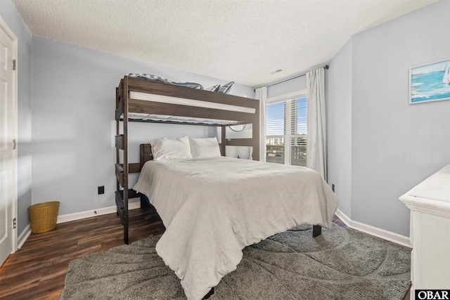 bedroom with a textured ceiling, dark wood finished floors, and baseboards