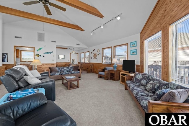 living room with beamed ceiling, wood walls, wainscoting, and visible vents