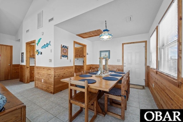 dining area with a wainscoted wall, light tile patterned flooring, vaulted ceiling, and wood walls