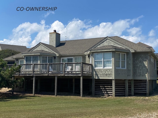 back of property with a deck, roof with shingles, a lawn, and a chimney