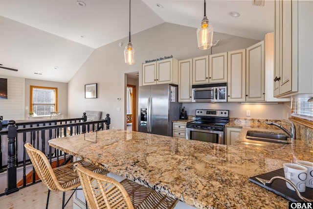 kitchen featuring stainless steel appliances, a sink, cream cabinetry, light stone countertops, and a kitchen bar