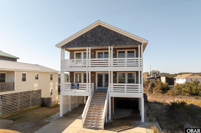 raised beach house featuring concrete driveway, stairway, an attached garage, french doors, and a carport